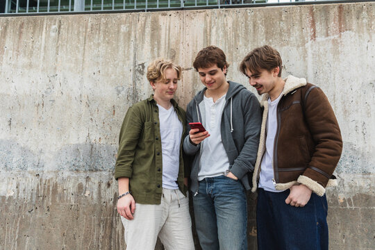 Friends Looking at Smartphone by Concrete Wall