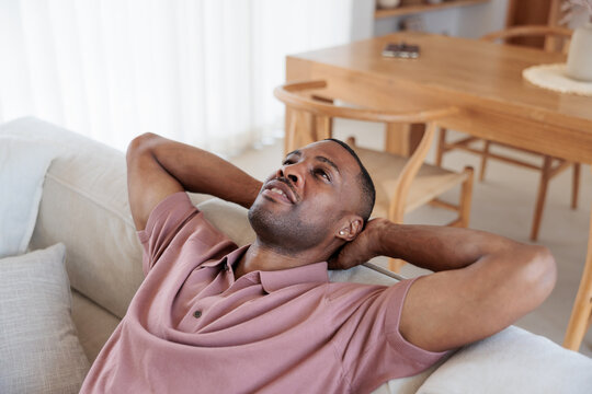 Man relaxing on couch, looking up, hands behind head.
