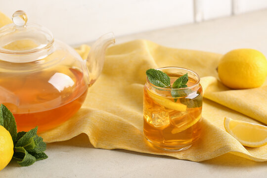 Glass and teapot of lemon ice tea with mint on white background, closeup