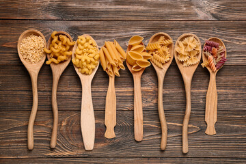 Naklejka premium Wooden spoons with different types of pasta on wooden background