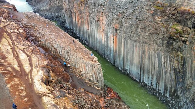 Aerial view of Studlagil Canyon with its unique basalt columns and turquoise river with people walking on the rocky edge in Eiriksstadhir, Mulathing, Iceland.