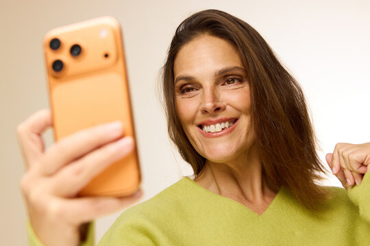 Smiling Woman Takes Selfie With Orange Phone in Bright Setting
