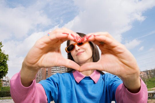 Young person shows heart shape with hands in colorful spring setting