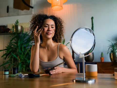 Woman applying coffee scrub while looking in mirror 