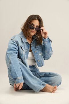 Woman in Denim Outfit Sits on the Floor and Poses for a Picture