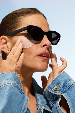 Woman Applying Skincare While Wearing Sunglasses Outdoors