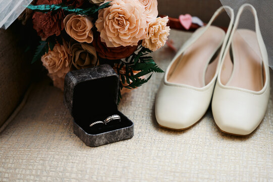 close up of ring in box and flat women's shoes and bouquet at wedding 