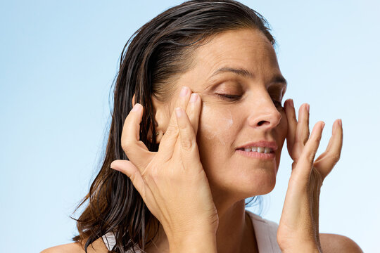 Woman Applying Skincare Product on Her Face in Studio Setting