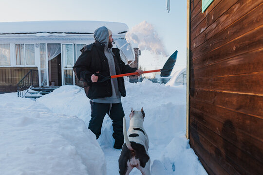 Man Shovels Snow in Front of House While Dog Watches Nearby in Winter