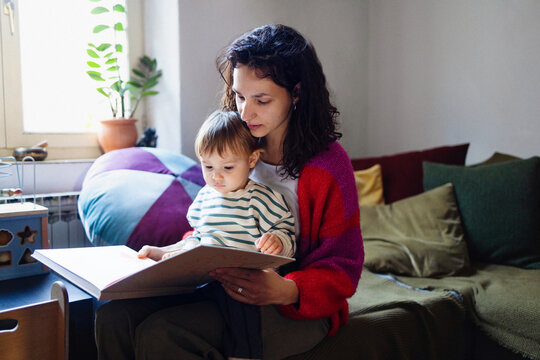 Mother Reading With Toddler On Sofa At Home