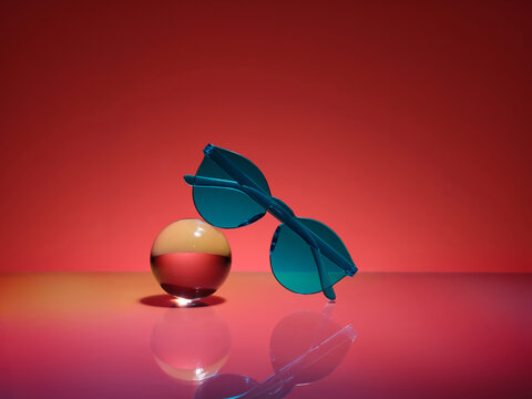 Modern teal sunglasses on a clear glass sphere with red backdrop