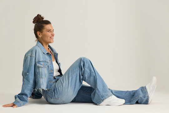 Woman Sitting on the Floor in Denim Outfit With Simple Background