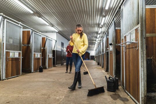 Woman Sweeping Stable Floor in a Professional Facility