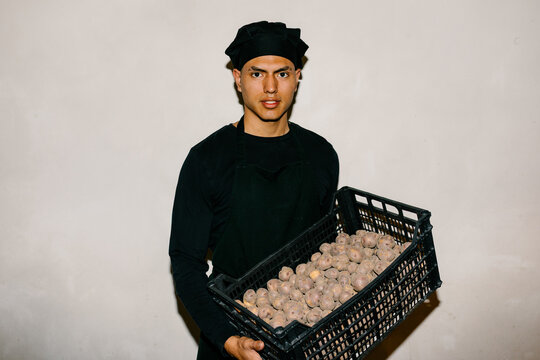 Portrait of a young chef holding a plastic crate of organic potatoes
