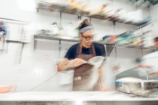 Baker sifting flour in a professional kitchen with motion blur