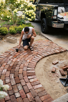man using rubber mallet to secure bricks of a small walkway to house