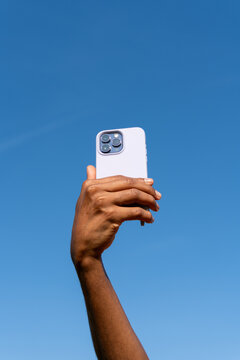 Hand Holds Phone Against Clear Blue Sky 