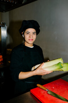 Portrait, lit with direct flash, of a female chef holding fresh leeks