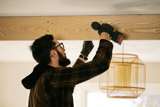 man wrapping old beam with white oak slabs inside his home