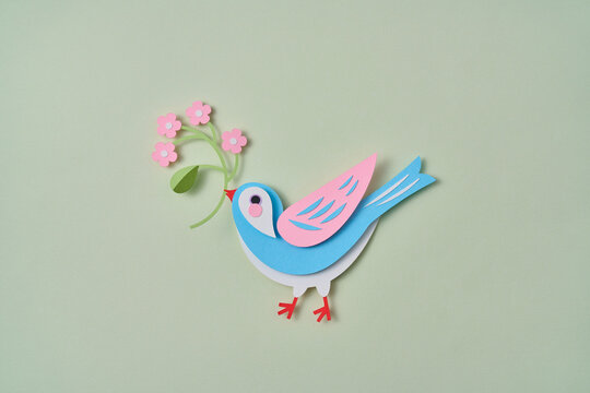 Paper spring craft bird hold flower on green