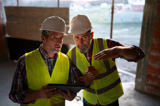 Two construction workers discuss plans indoors