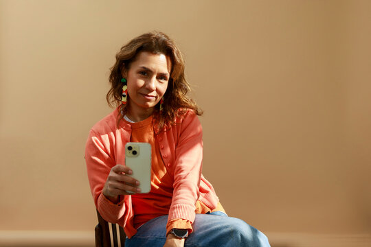 Woman Takes Selfie While Seated Against a Beige Background