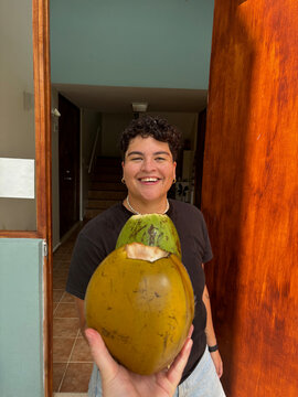 Smiling latin woman holding coconut out in the doorway  