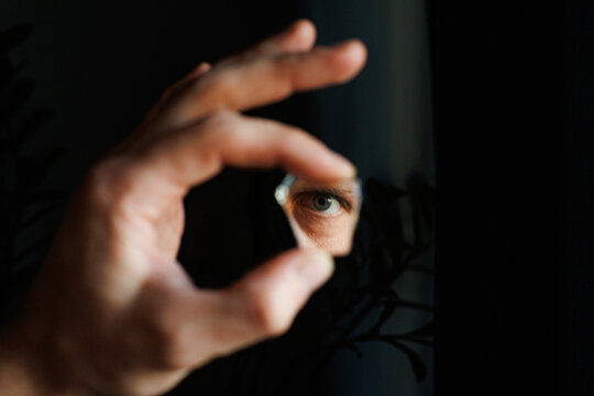Person Looks Through Piece Of Mirror in Dark Background Indoors