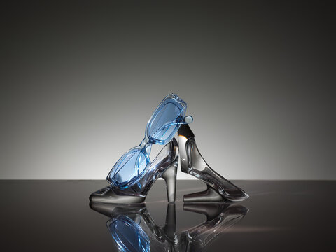 Glass high heel shoe with blue sunglasses, elegant fashion concept