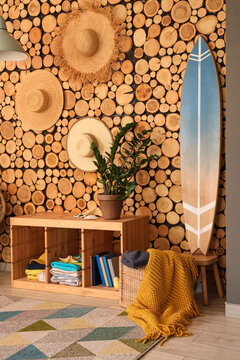Stylish interior of living room with houseplants, straw hats and surfboard. Summer composition
