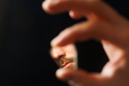 Person Looks Through a Small Broken Mirror in a Dark Background