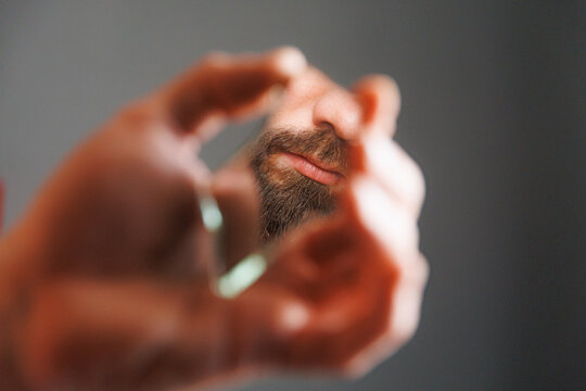 Man Holds Small Mirror Showing Part of His Face in Close View