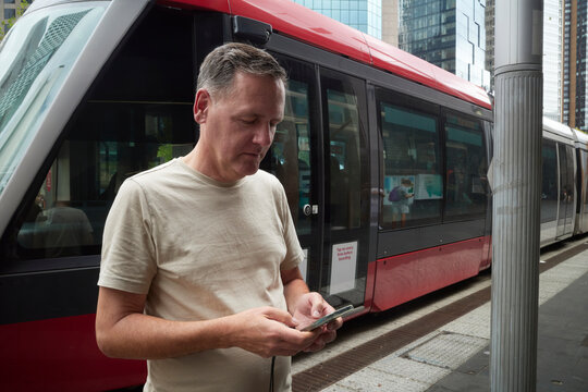 Man Using Phone While Waiting for Tram in Sydney