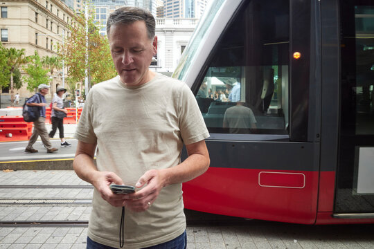 Man Using Mobile Phone Near Tram at a Busy City Street