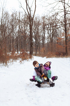 Young girl and boy on a sledge sliding down and having fun in the snow