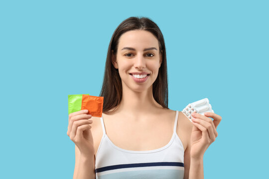 Beautiful young woman with birth control pills, vaginal suppositories and condoms on blue background