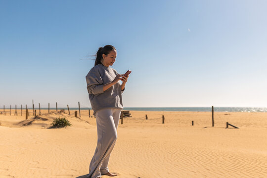 Woman using mobile phone on beach under blue sky