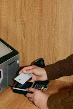 Hand holding credit card over payment terminal at checkout