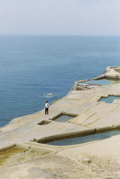 Isolated figure standing by salt pans overlooking the sea