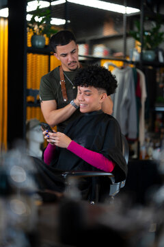 Barber cuts hair while client checks phone