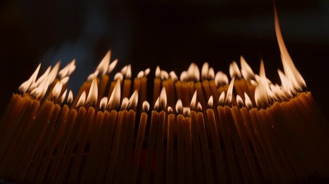 Rows of warm candle flames in a dark temple setting create a sacred visual composition with glowing light, soft smoke, and peaceful Buddhist worship atmosphere.