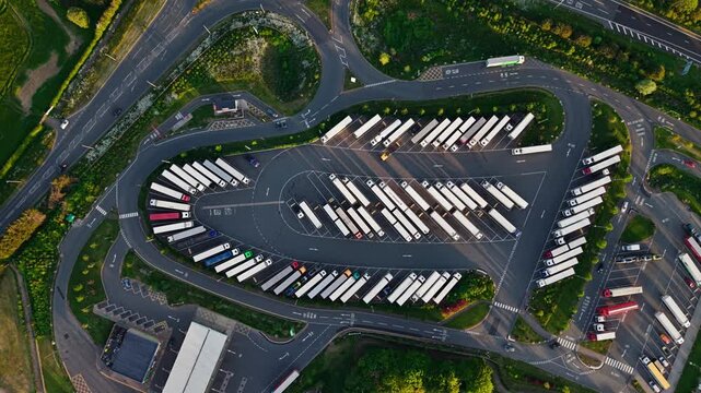 Aerial view of Rugby Services showing rows of parked trucks and lorries surrounded by green trees and access roads during golden hour in Rugby, England, United Kingdom.