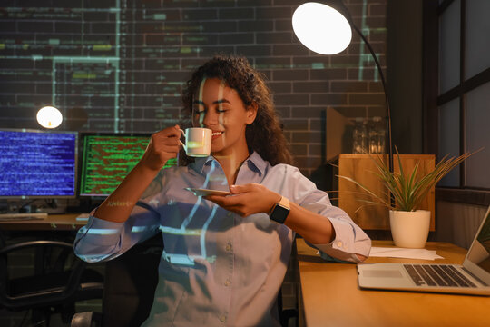 Female African-American programmer drinking coffee in office at night
