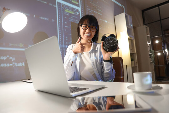 Young female programmer with alarm clock in office at night