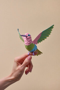 Paper hummingbird held between fingers, beige