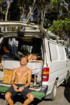 Man sunbathing at back of camper van while woman rests inside.