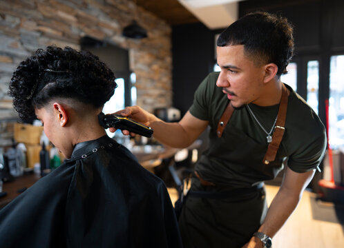 Barber gives haircut in a busy shop in the morning