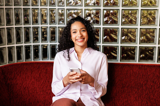Woman portrait holding smartphone on red sofa indoors