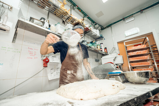 Baker dusting flour on fresh dough in bakery