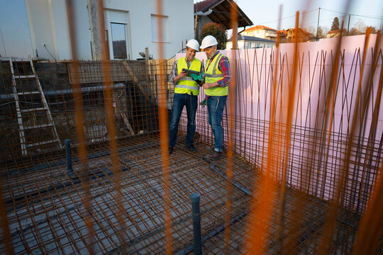 Two workers check plans at a construction site